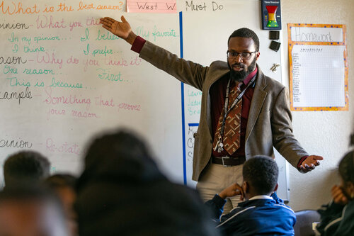 A teacher presenting written information on a whiteboard to a class full of students 