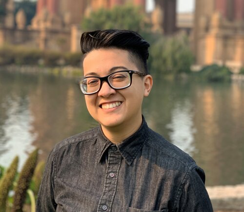 A portrait of Marissa Chavez smiling in a dark button-up shirt in front of the Palace of Fine Arts