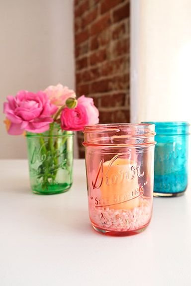 Three colored Mason jars with flowers and candles inside of them