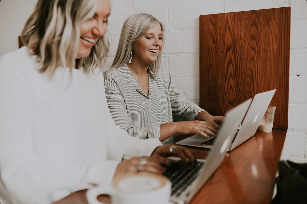 Two people typing on laptops and smiling 