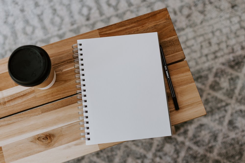 a blank notebook, a pen, and a to-go coffee on a table
