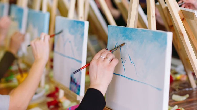 A row of people painting on canvases on easels 