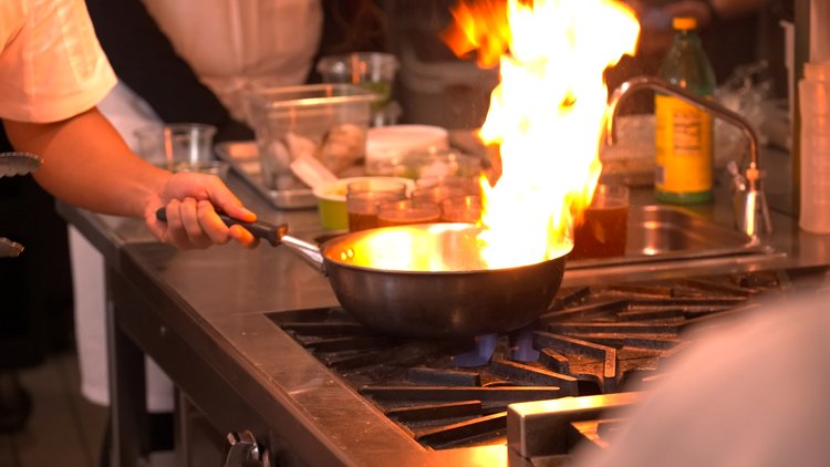 Someone cooking while a flame erupts from a pan on a stove