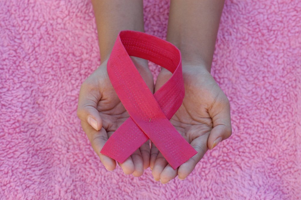 two hands holding a pink breast cancer awareness ribbon while resting on a pink sherpa blanket