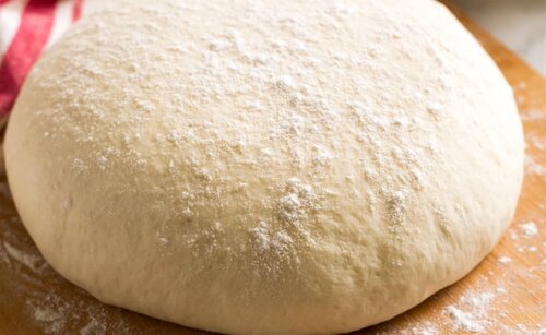 A ball of lightly flowered pizza dough on top of a wooden surface