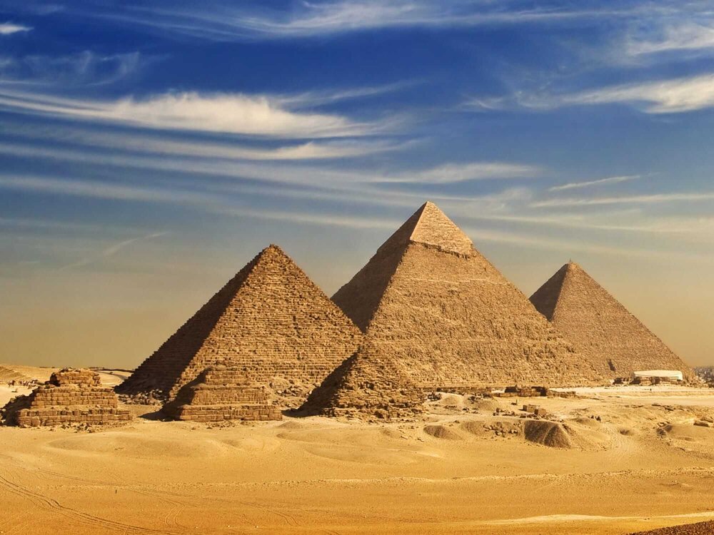 Six Egyptian pyramids with deep blue skies and clouds behind them
