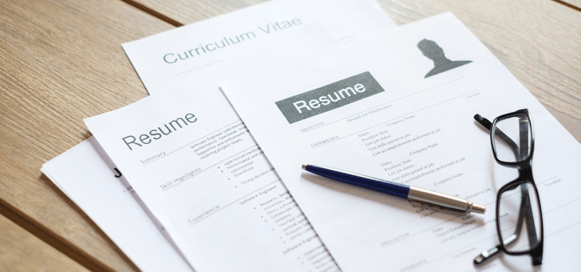 A stack of resumes, a pair of glasses, and a pen