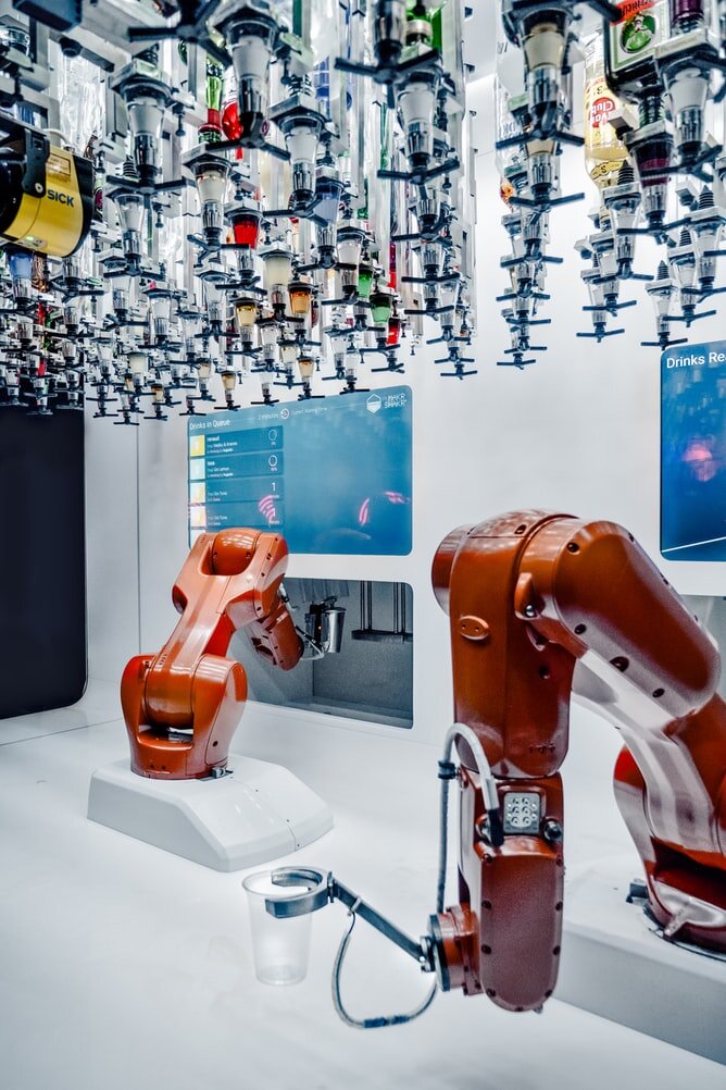 Two orange single-arm robots in front of large lit-up computer screens in a white room