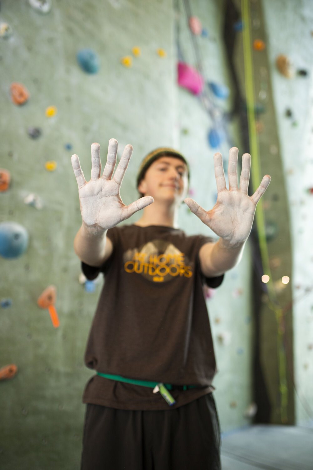 Person with their chalk-covered hands out in front of them while in front of a rockwall 