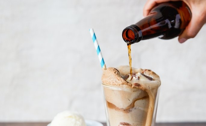 Someone pouring a bottle of root beer into a root beer float