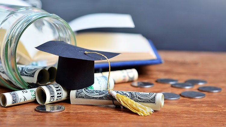 A miniature grad cap on top of a pile of rolled cash and coins