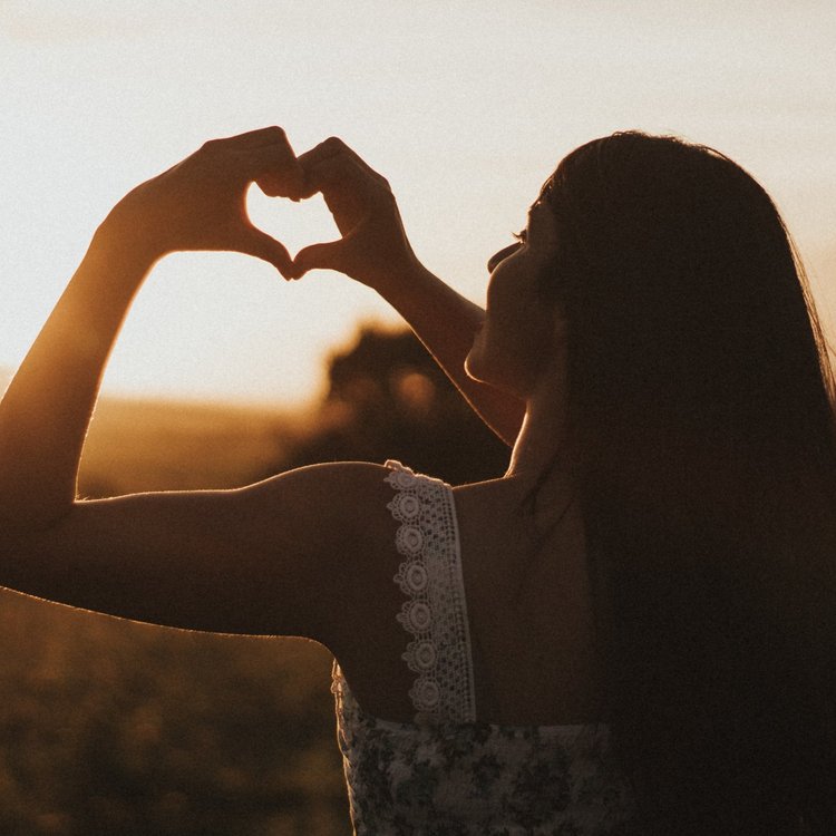 Someone smiling while forming a heart shape with their fingers