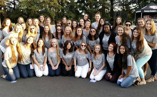 A large group of sorority members standing in rows and smiling while wearing sorority t-shirts