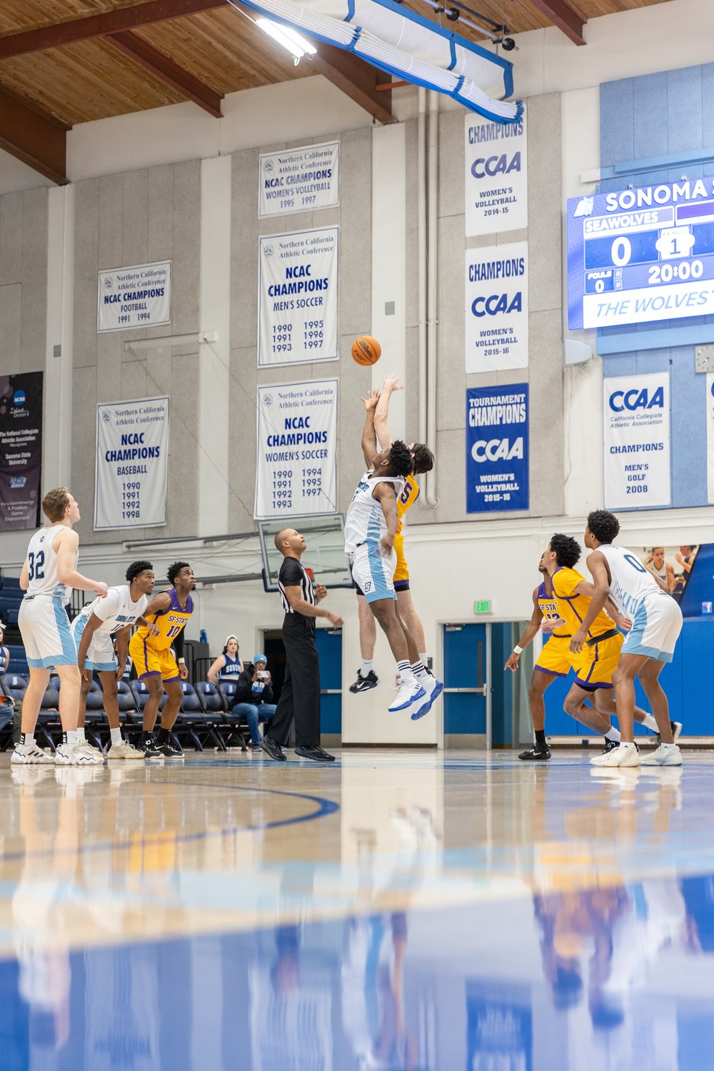 A player from Sonoma State's Men's Basketball team leaps in the air to fight an opposing player to score a basket.