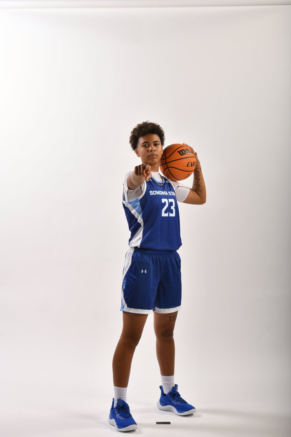 Sonoma State University Women's Basketball player Eryn Gardner holding a basketball in one hand and pointing at the viewer with the other