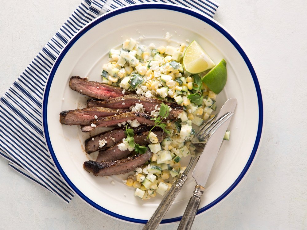 A plate of steak garnished with corn and slices of lime
