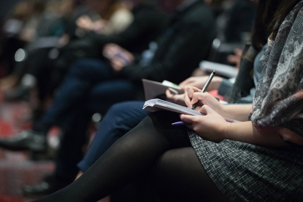 a row of students in a lecture hall with the student in focus taking notes