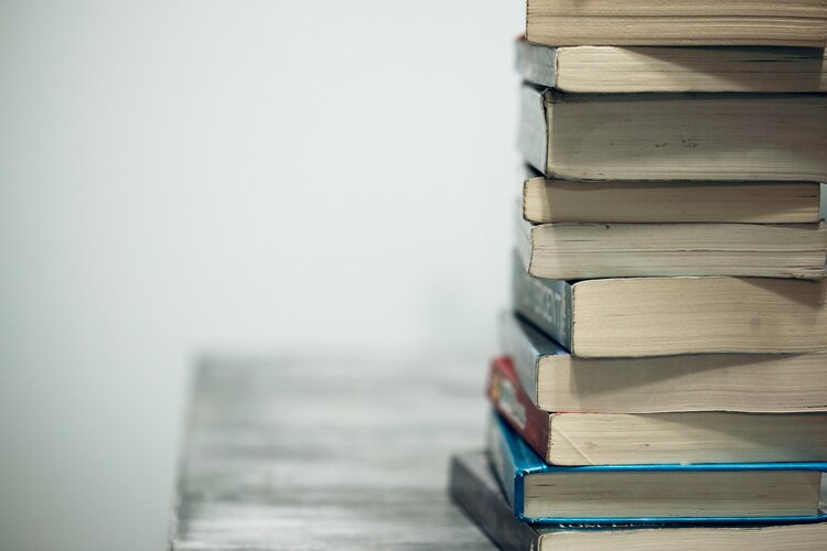 Multi-colored books stacked on a wooden surface in front of a white background