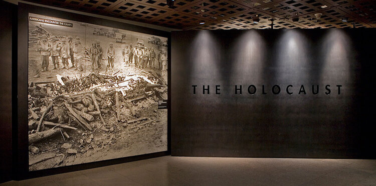 Low-lit area of the U.S. Holocaust Memorial Museum featuring a large photograph and the words "The Holocaust" under artistic lighting