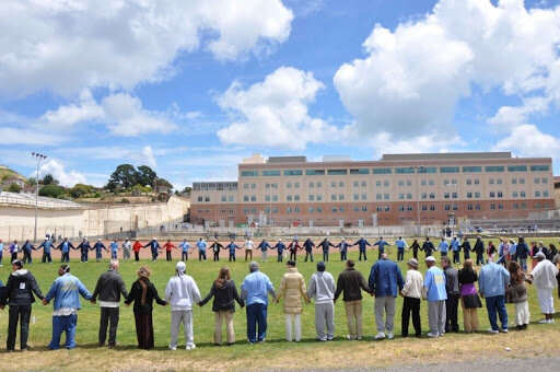 A large group of people standing in a circle and holding hands in an outdoor setting