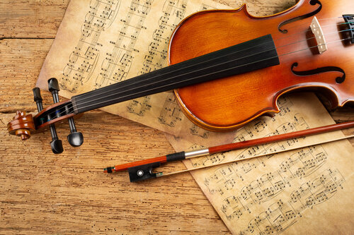 A violin laying on top of some weathered music manuscripts 