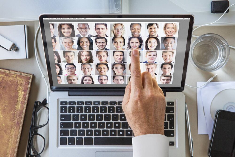 A hand pointing to the screen of a laptop featuring multiple images of different people's faces 