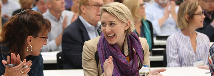 A group of people talking and smiling in a crowded and seated indoor setting 