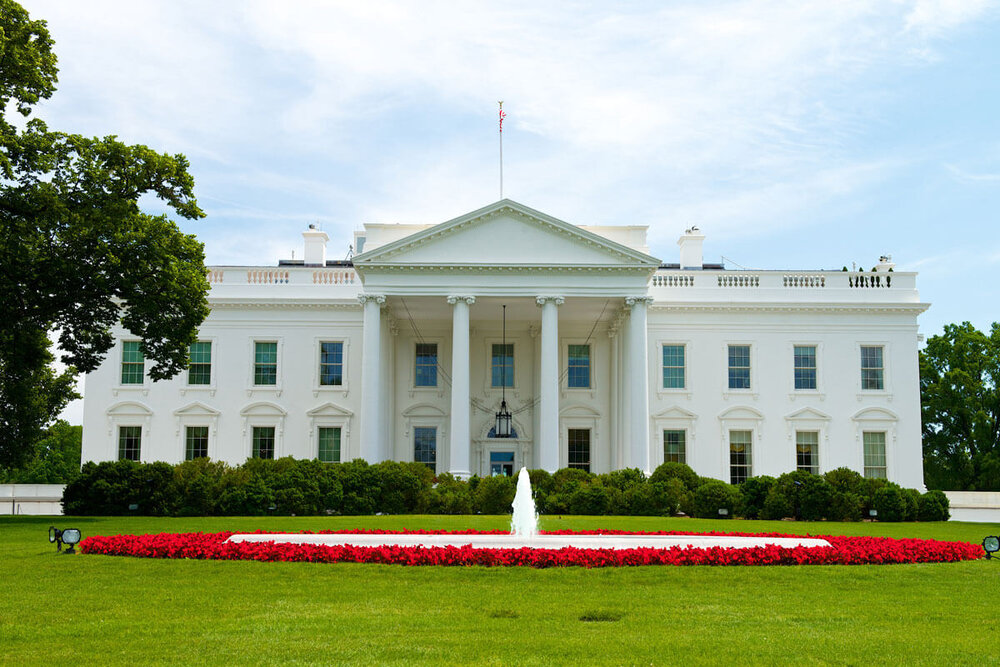 The White House with a fountain shooting water in the front surrounded by red flowers