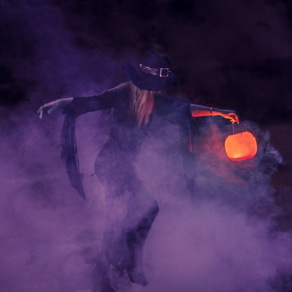 a witch holding a jack-o'-lantern surrounded by purple smoke