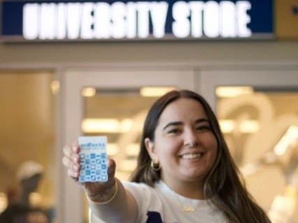 A student smiling while holding up a Wolfbucks card 