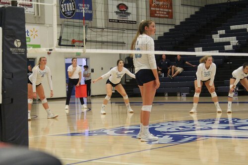 People on the women's volleyball team playing volleyball in an indoor setting