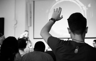 A black and white image of someone raising their hand to ask a question in a group setting