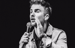 A black and white image of DJ Demers performing a comedy set