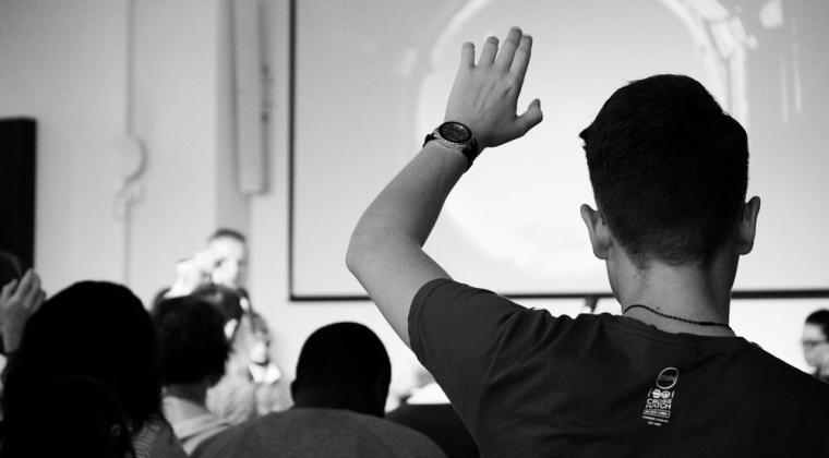 A black and white image of someone raising their hand to ask a question in a group setting