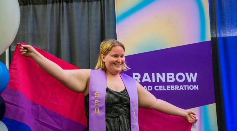 A student smiling and posing for a photo at Rainbow Graduation