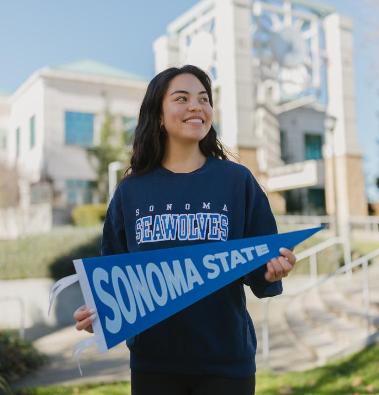 Student holding a SSU pennant in front of the library