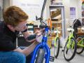 A person with red hair and safety glasses on using an electric tool on a blue bicycle 