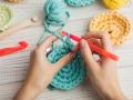 Hands crocheting with teal yarn and red crochet hooks