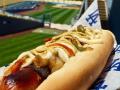 A condiment-covered hot dog with a baseball field in the background 