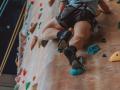 Person climbing indoor rock wall in blue t-shirt and grey shorts