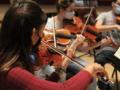 People playing violins while wearing masks in an indoor setting