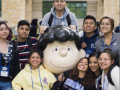 A group of students wearing name tags smiling and posing around the Lucy statue 