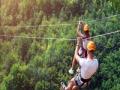 Two people ziplining over a forest of tree tops 