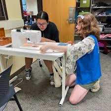 Someone helping someone else learn to sew