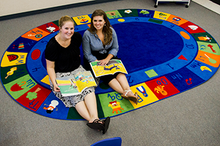 two student teachers sit on a colorful rug
