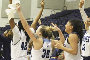 women's basketball players celebrate with arms in the air